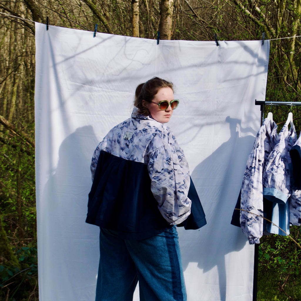 lightweight sustainable bomber jacket for women with blue and cream cloud print and navy contrast. long sleeves, elastic cuffs, collar, zip closure and breast pocket, oversized fit. casual spring summer jacket for women