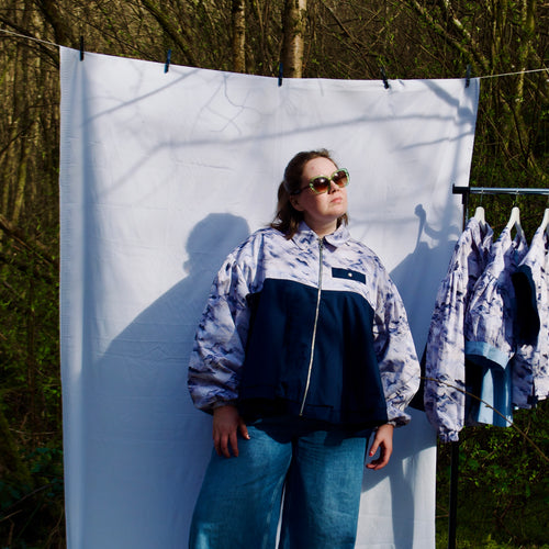 lightweight sustainable bomber jacket for women with blue and cream cloud print and navy contrast. long sleeves, elastic cuffs, collar, zip closure and breast pocket, oversized fit. casual summer jacket for women